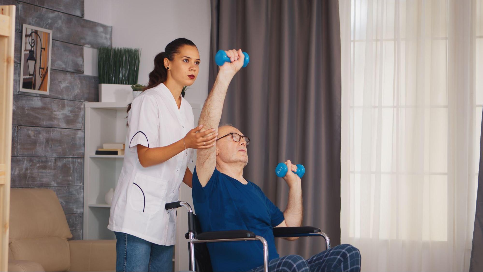 therapist helping individual on wheelchair with hand exercise using dumbbell